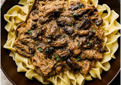 Beef stroganoff with noodles in brown bowl.